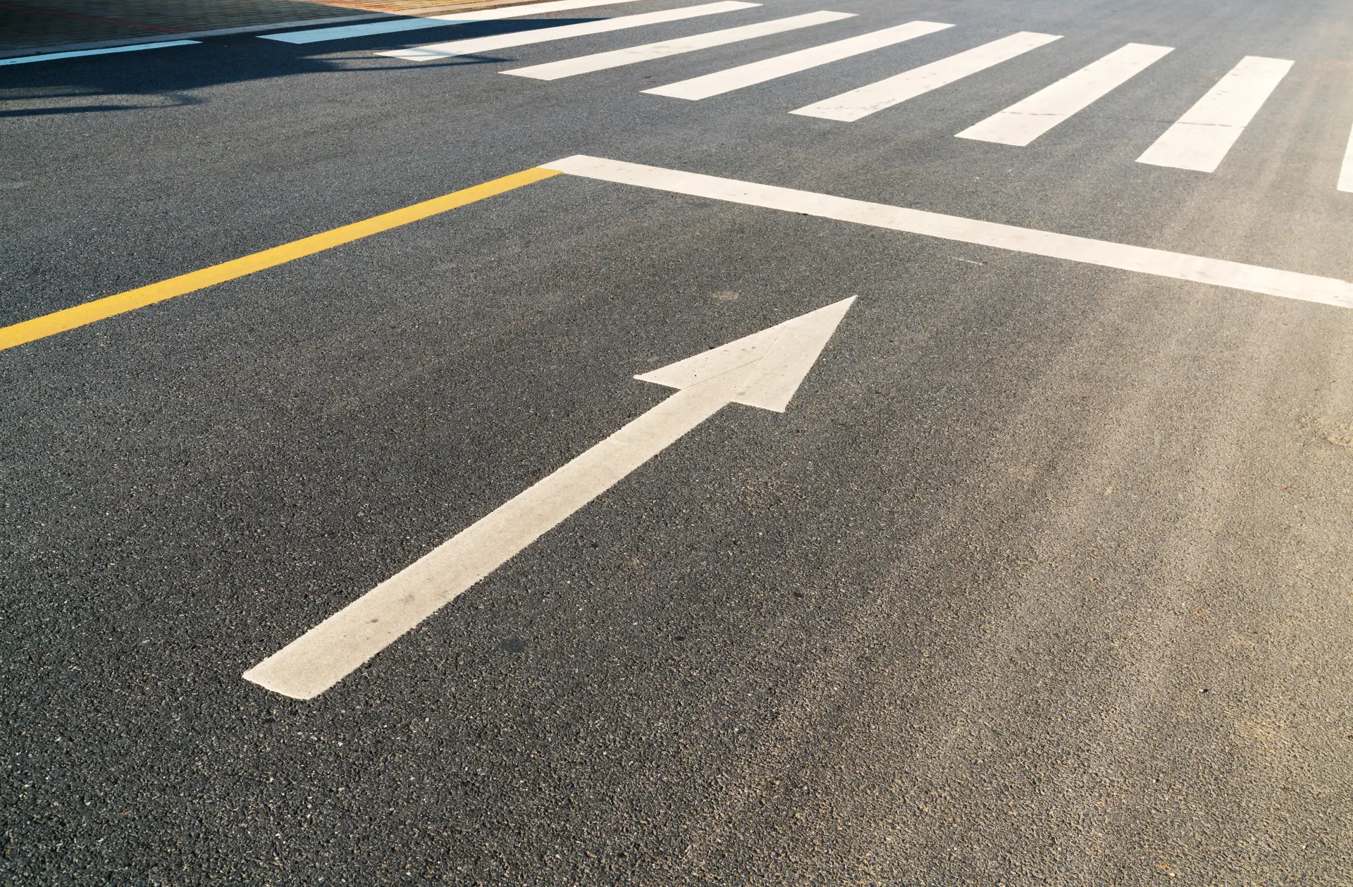A wide angle shot of a road, focusing on a directional arrow by a crosswalk